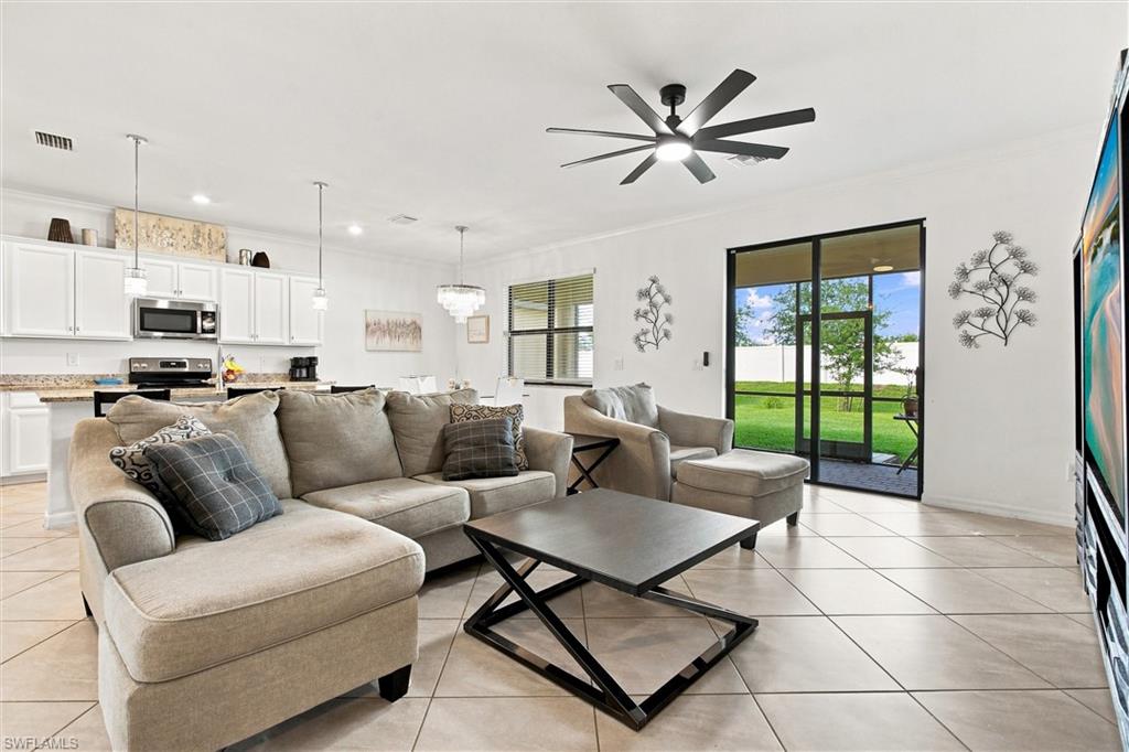 Open-plan living room with beige sectional, white kitchen, tiled floors, and sliding doors to the lawn.