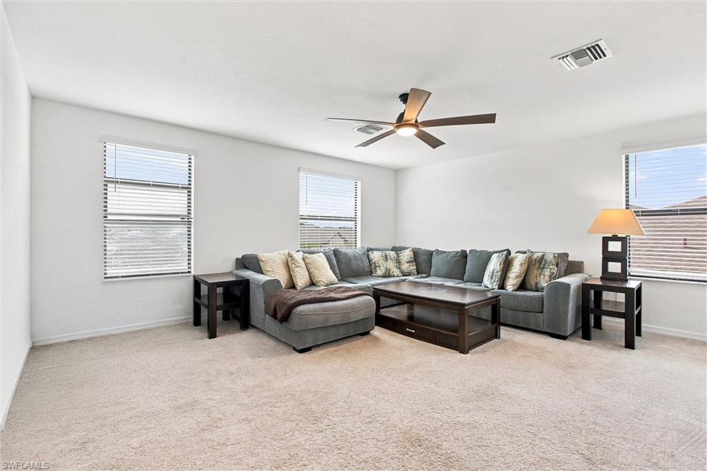 Living room with a gray sectional, dark wood tables, ceiling fan, and three windows with blinds.