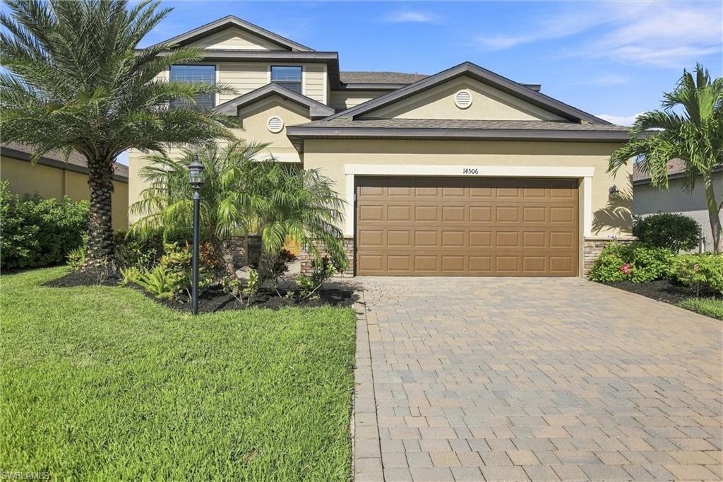 Two-story beige home with a brown double garage, palm landscaping, and a wide paver driveway.
