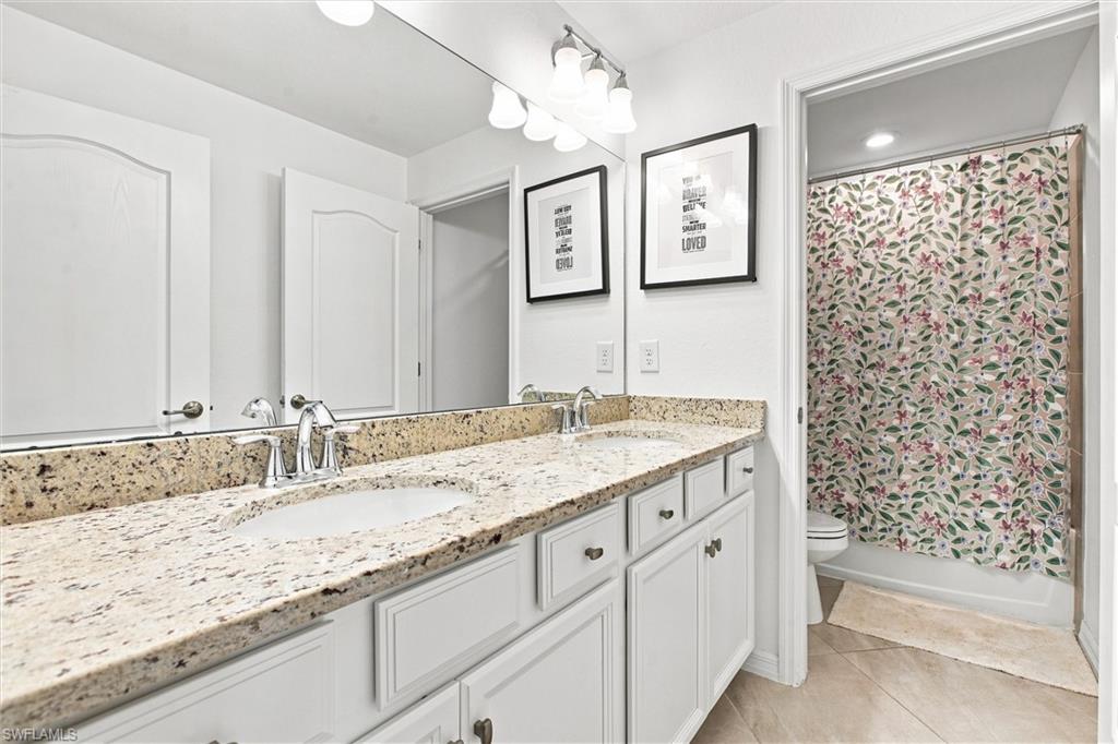 Bathroom with granite double vanity, white cabinetry, and a floral shower curtain.