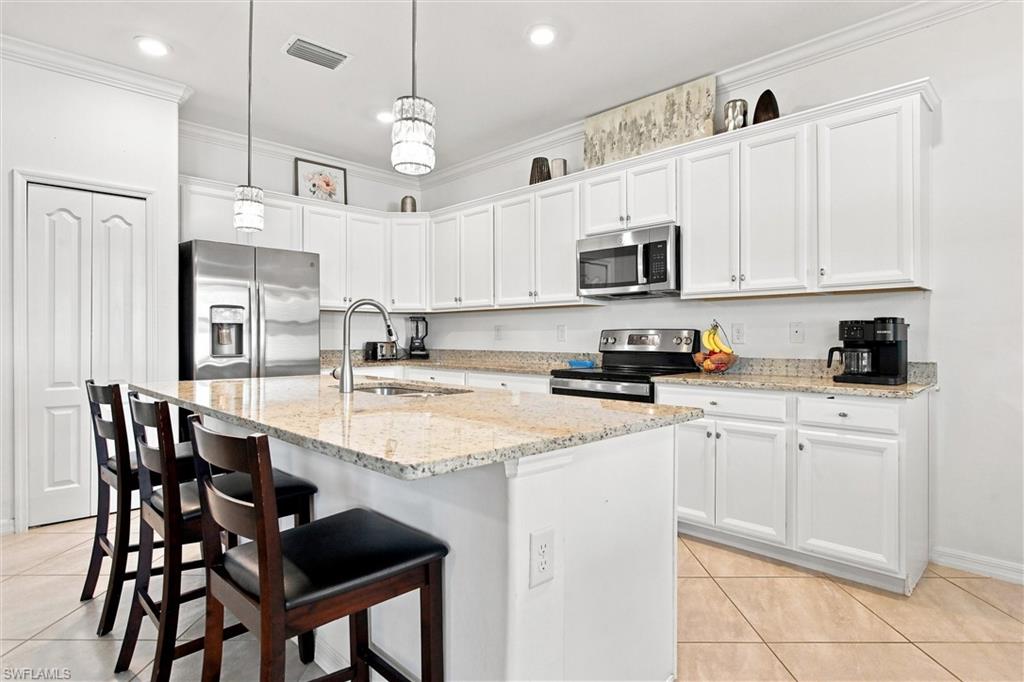 Kitchen with white cabinets, granite island, stainless steel appliances, and dark wood bar stools.
