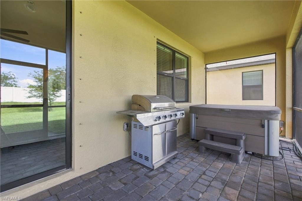 Covered patio with a stainless steel grill, covered hot tub, and paver flooring.