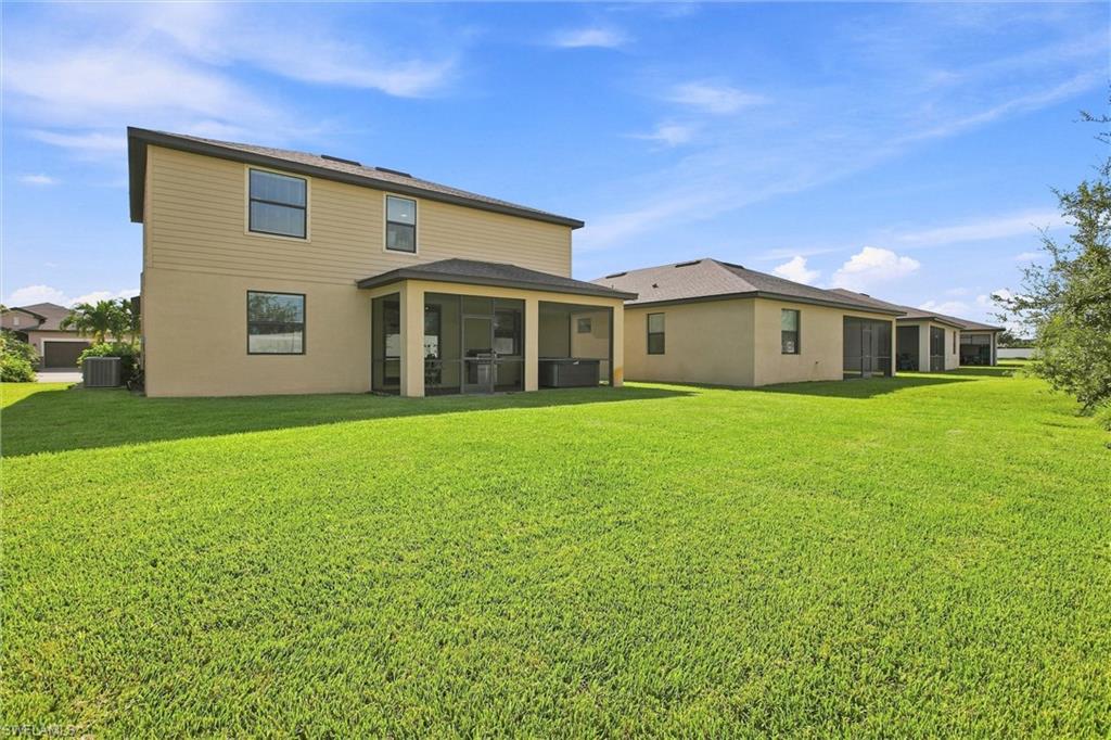Two-story beige home with a covered rear patio and broad green lawn.