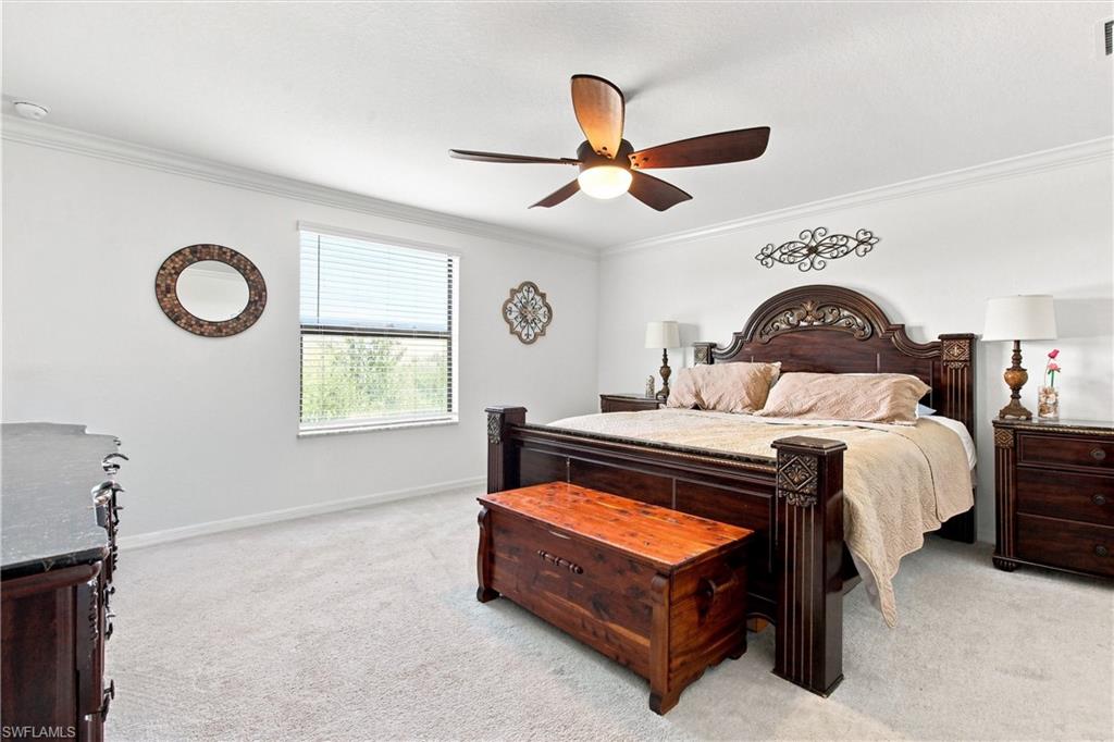Bedroom with a carved dark-wood bed, storage chest, ceiling fan, and carpet.