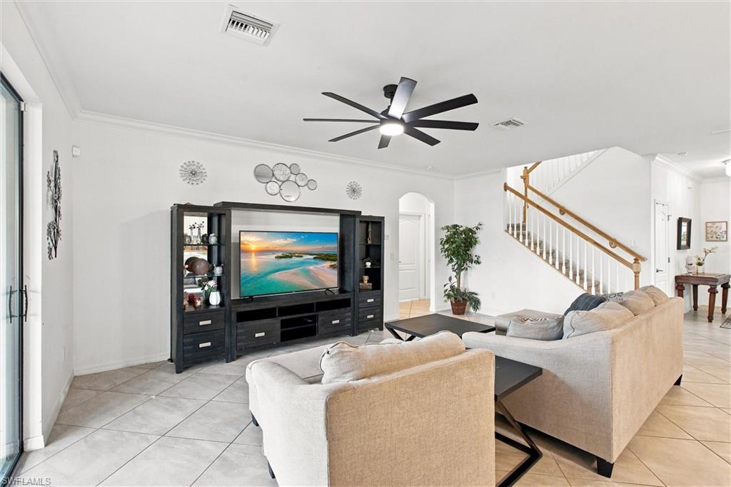 Furnished living room with pale sofas, a black entertainment center, and a staircase with a wood handrail.