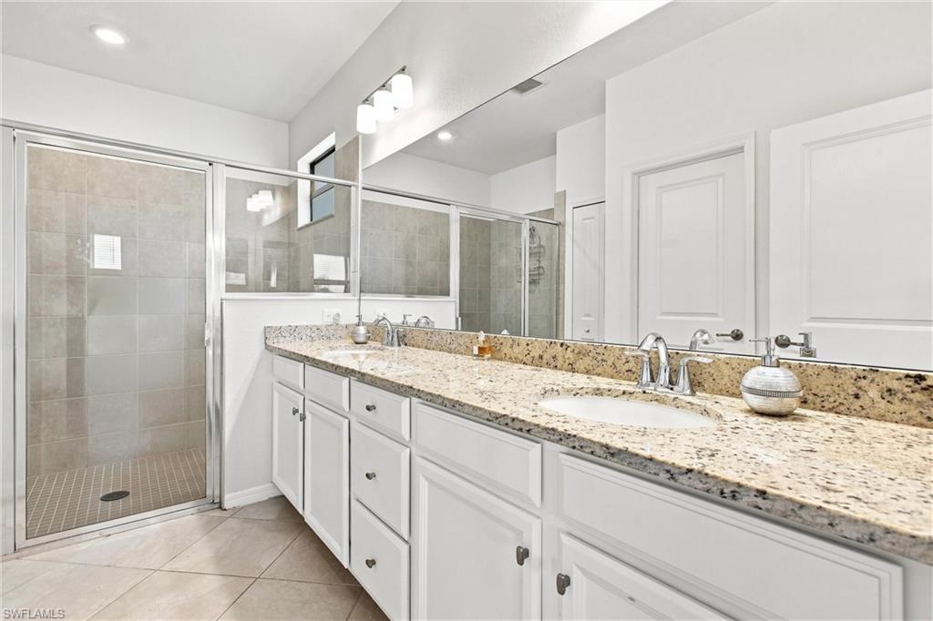 Bathroom with a granite double-sink vanity and glass-enclosed tiled shower.