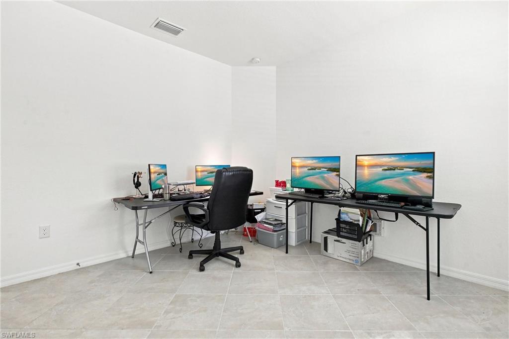 Home office with two computer desks, multiple monitors, and a black swivel chair.