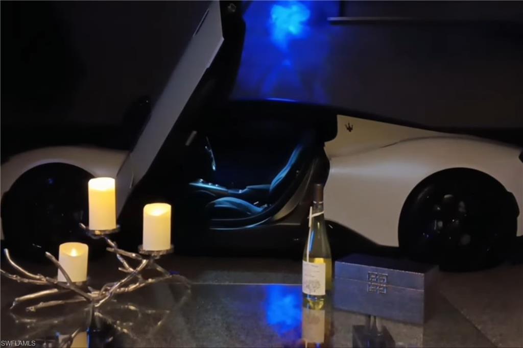 White sports car inside a dark garage, with blue lighting and candles in the foreground.