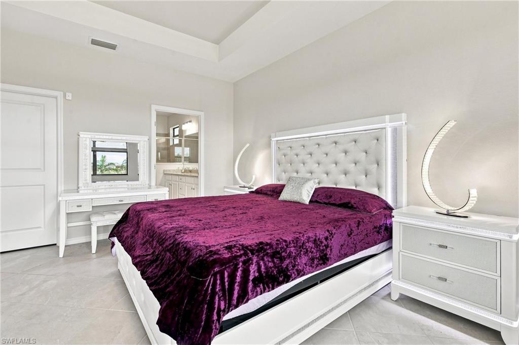 Bedroom with a large bed in purple bedding, tufted headboard, and white vanity.
