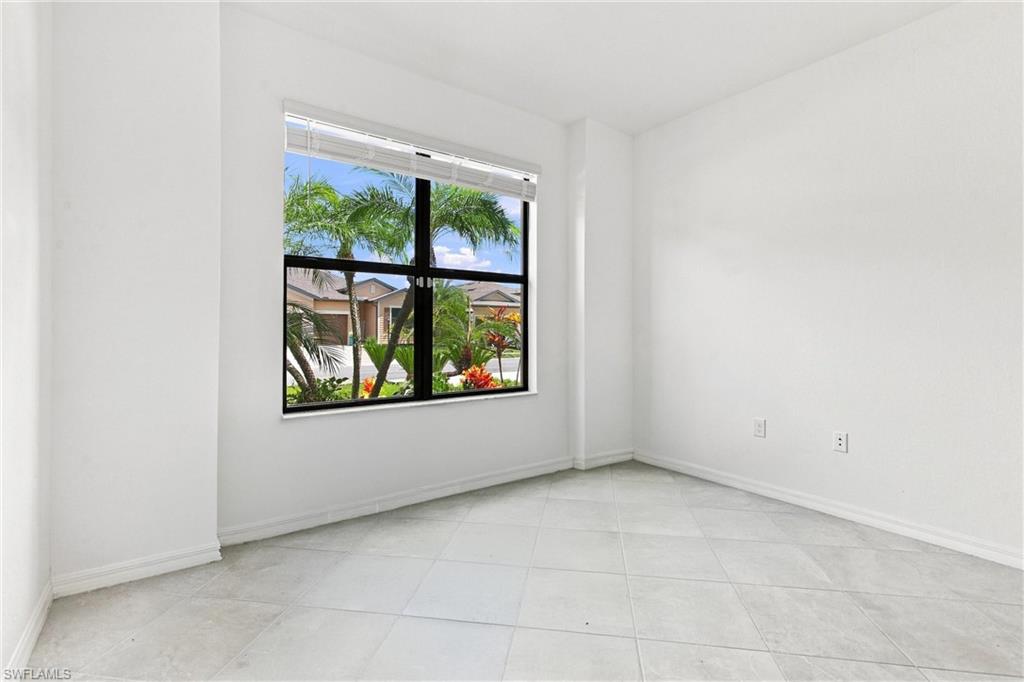 Vacant room with large tile floor and a window overlooking palm trees and neighboring homes.