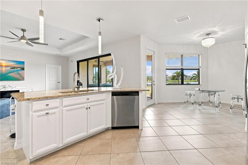 Open kitchen with granite island and white cabinets beside a glass dining table and window.