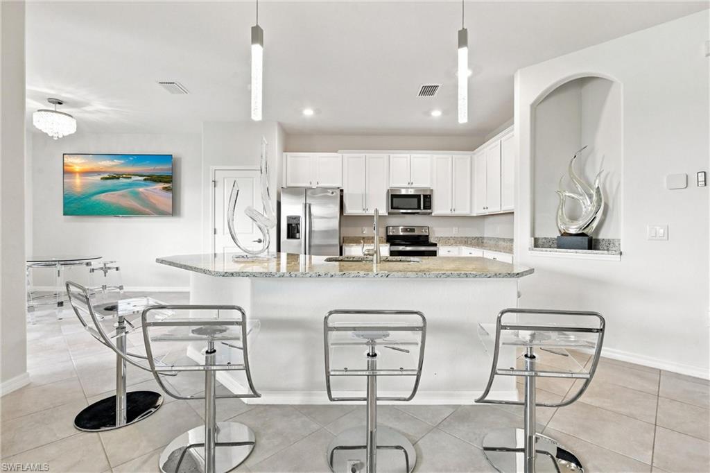 Modern kitchen with a granite island, white cabinets, stainless appliances, and chrome bar stools.