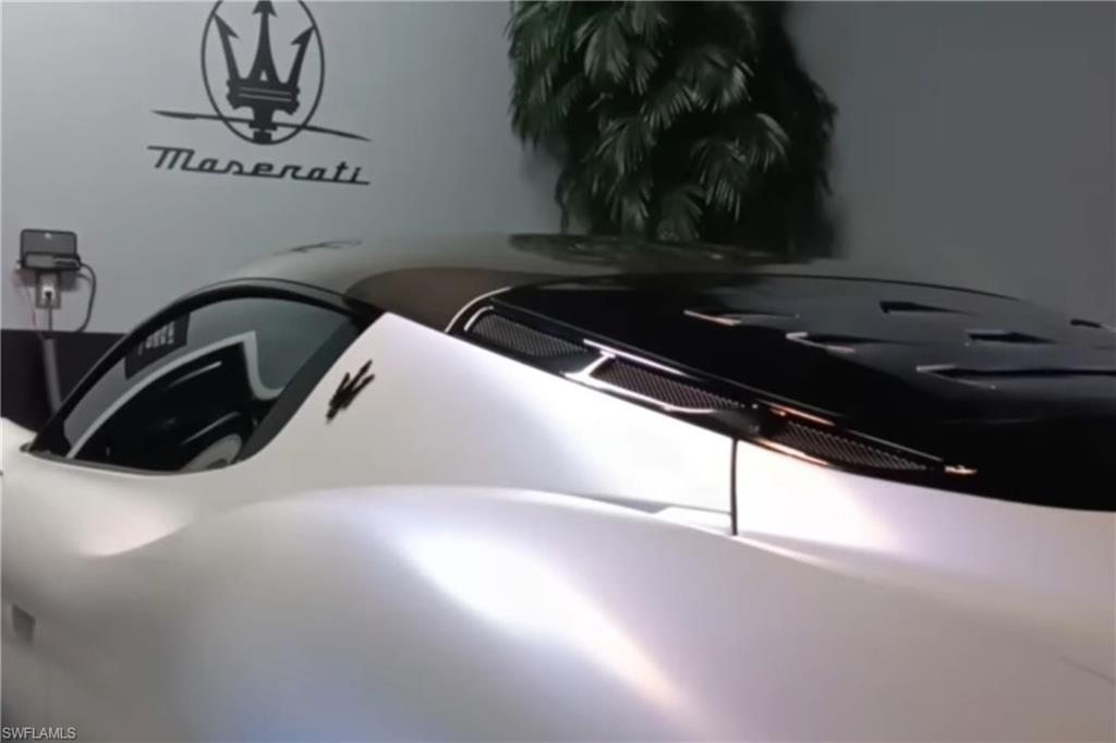 White Maserati sports car in a garage, with the Maserati emblem displayed on the wall.
