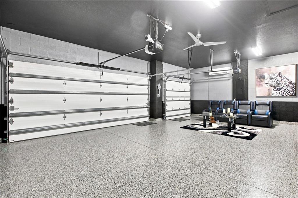Furnished garage with two overhead doors, a speckled epoxy floor, and a black-and-blue seating area.