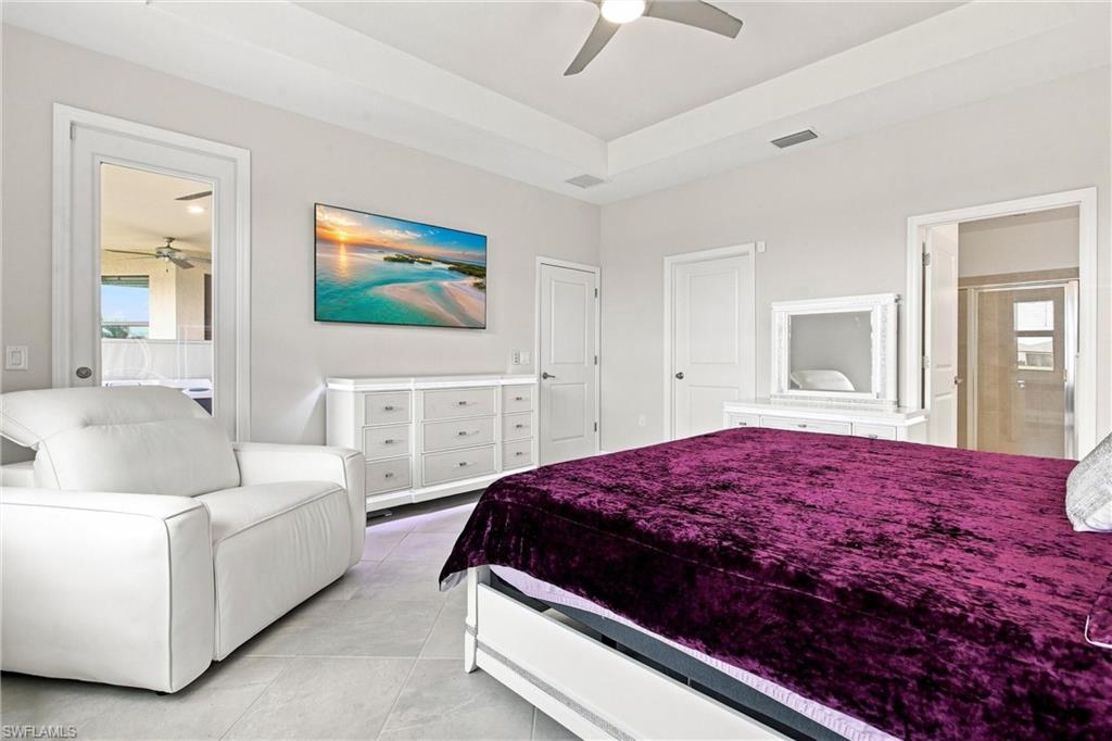 Furnished bedroom with a deep purple bedspread, white recliner, and framed beach picture.