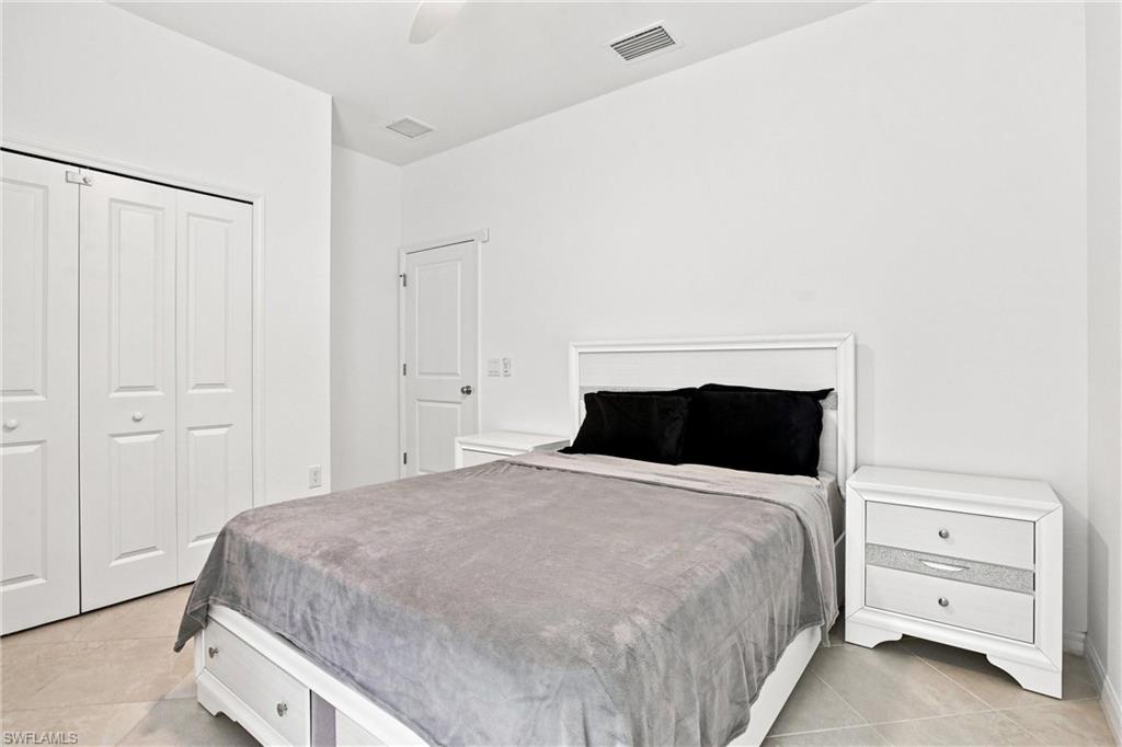 Bedroom with a gray bedspread, black pillows, white furniture, and tiled flooring.