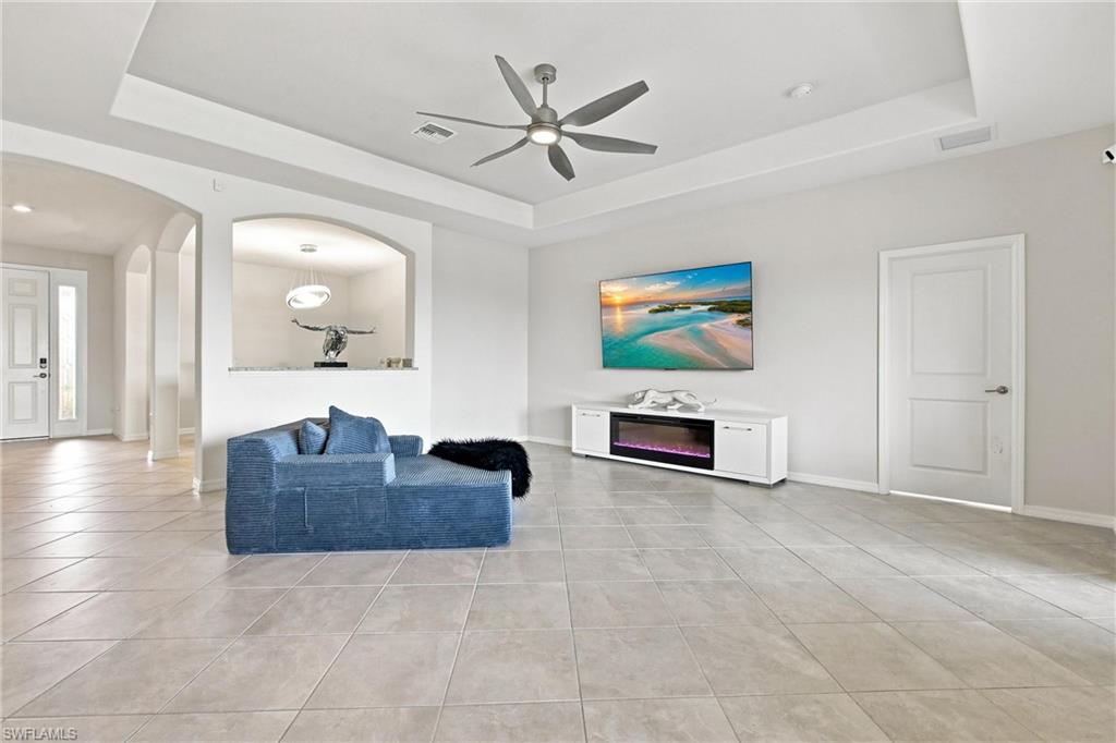 Furnished living room with blue sofa, tray ceiling, tiled floor, and white electric fireplace console.