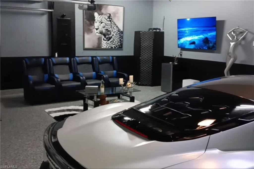 Car parked beside black theater seats and a wall-mounted television.
