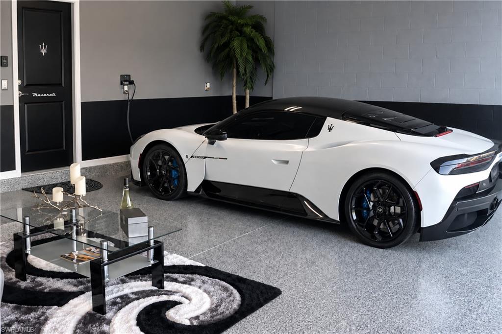 Finished garage with a white Maserati, polished gray floor, and a glass coffee table beside a patterned rug.