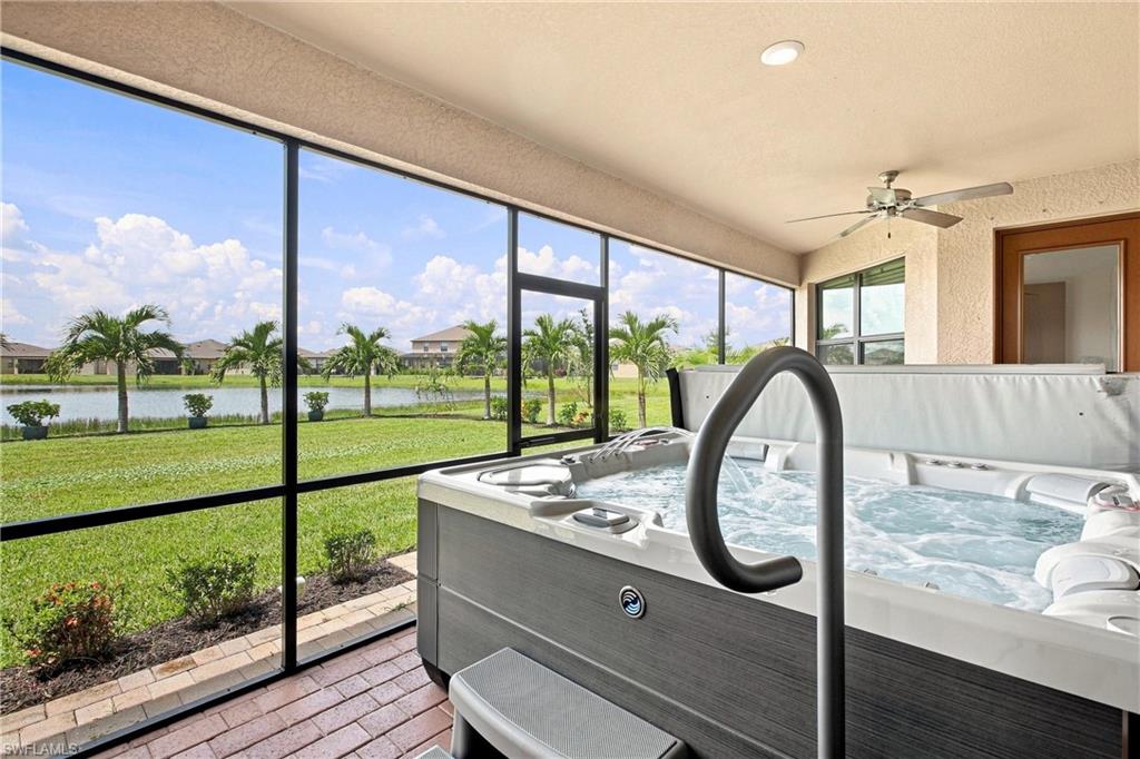 Enclosed lanai with a large hot tub overlooking a lake and palm-lined lawn.