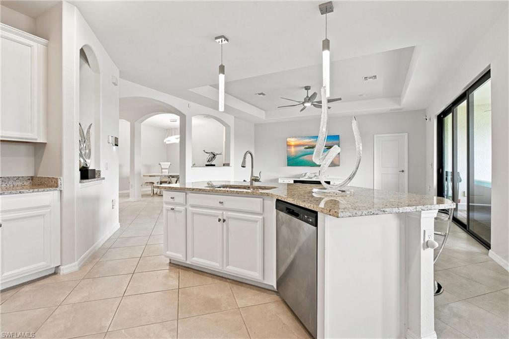 Open kitchen with a granite island, white cabinets, pendant lights, and arched openings to the dining area.