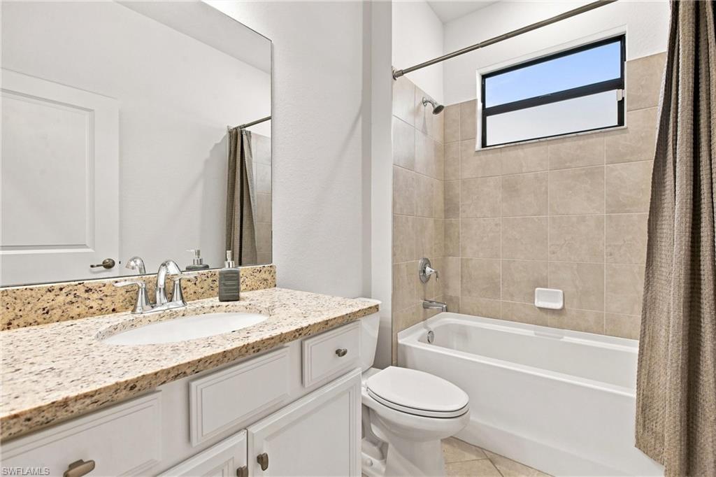 Bathroom with a granite-topped vanity, toilet, and tub beneath a high window.