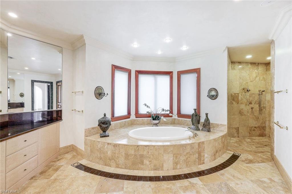 Marble bathroom with a built-in soaking tub beneath three windows and a walk-in shower.