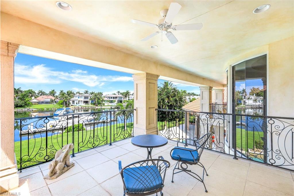 Covered balcony with wrought-iron railings and seating overlooking a canal and waterfront homes.