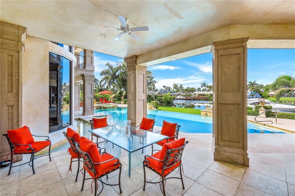 Covered patio with red-cushioned dining chairs beside a pool overlooking a canal.