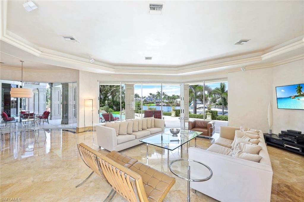 Living room with cream sofas and wide windows overlooking a pool, water, and palm trees.
