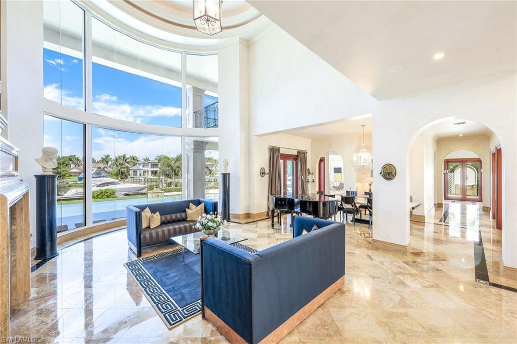 Living room with soaring curved windows, blue sofas, marble floors, and a canal view.