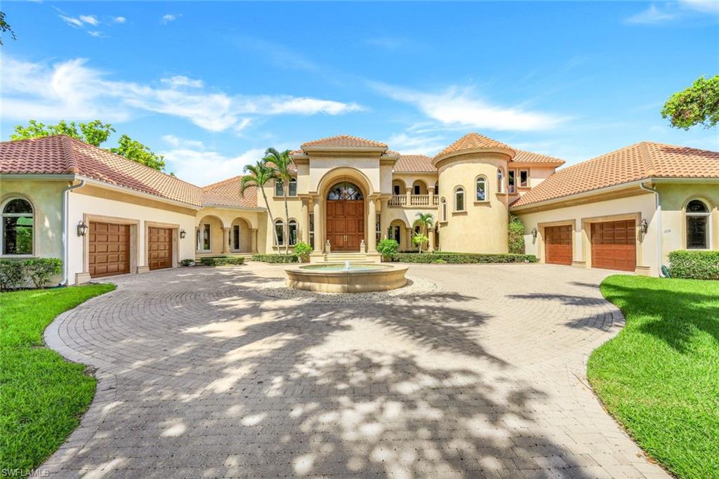 Mediterranean-style home with a round fountain, curved paver driveway, and multiple garage doors.