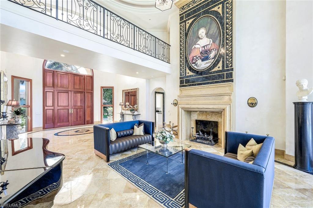 Two-story living room with blue sofas, a marble fireplace, and an ornate wrought-iron balcony.