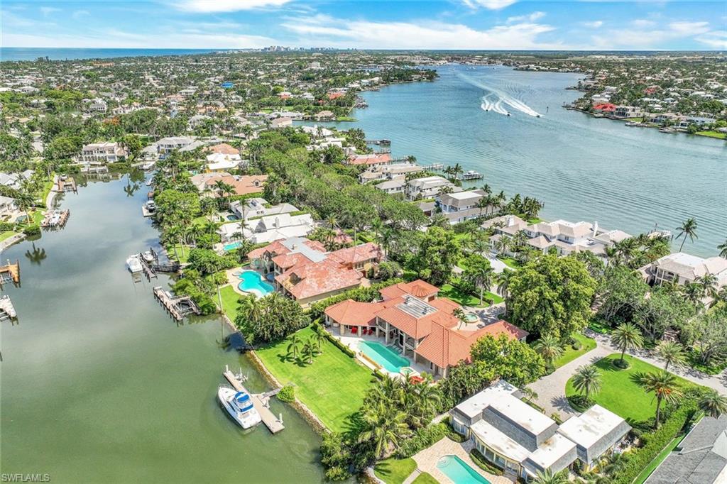 Aerial view of waterfront homes, pools, and docks beside canals and a broad waterway.