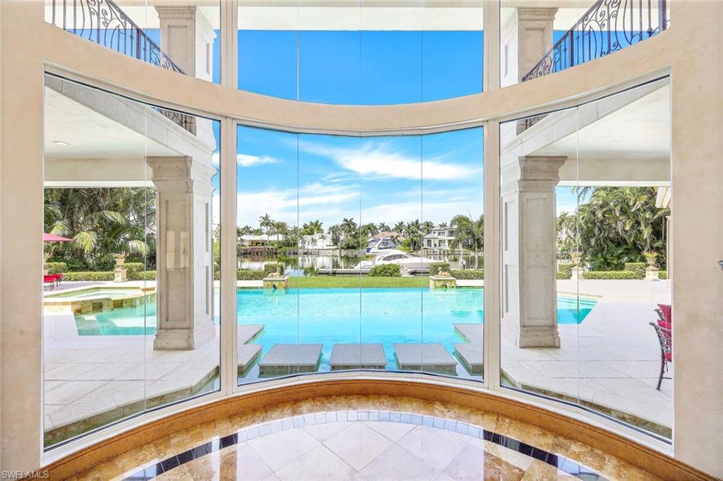 Curved floor-to-ceiling windows overlook a swimming pool, canal, and boat.
