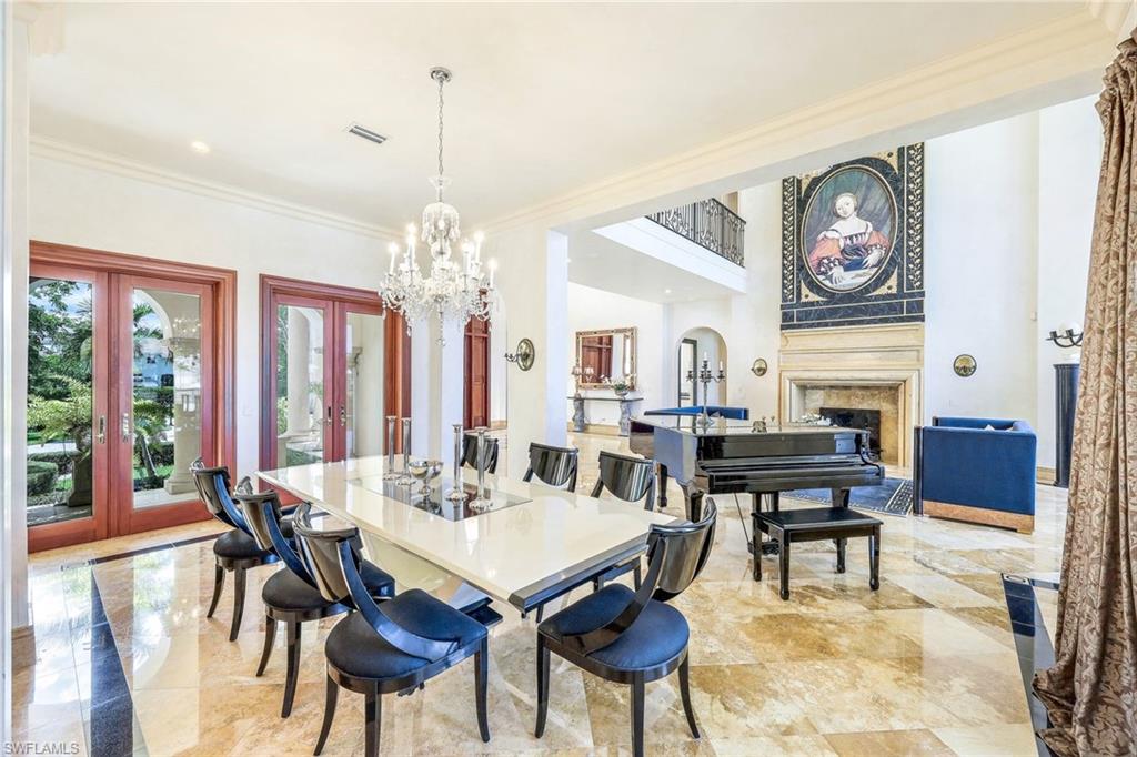 Formal dining room with a glass table and chandelier opening to a living room with a fireplace and grand piano.