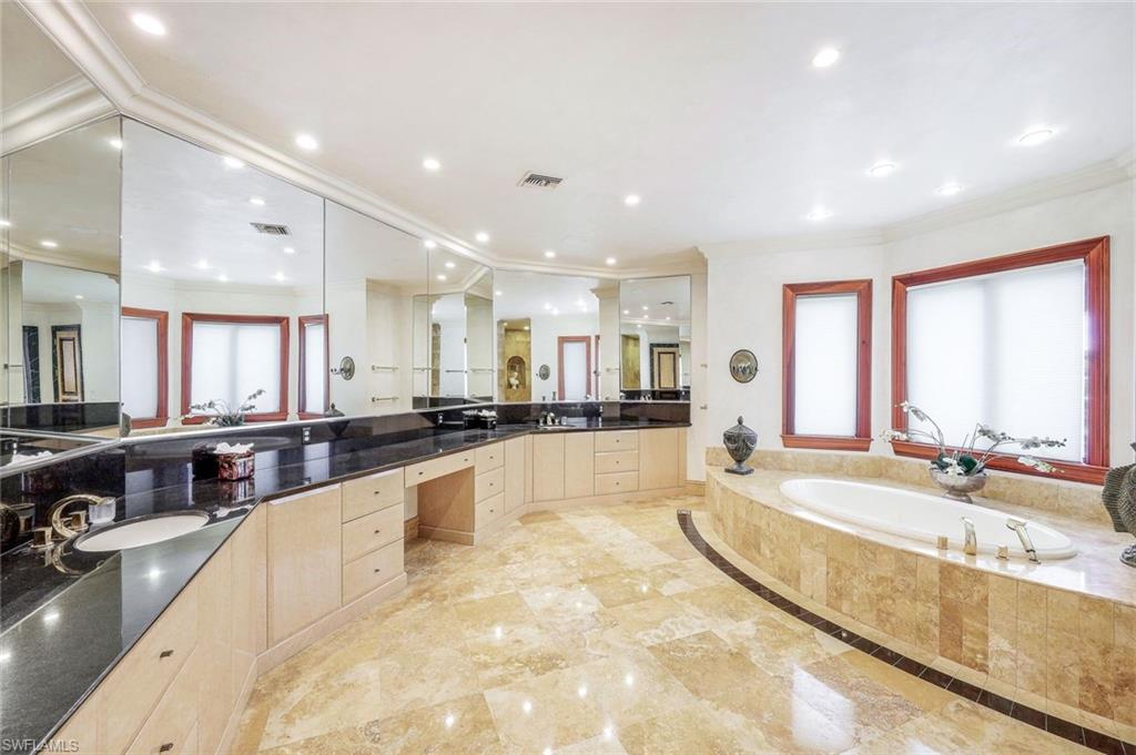 Spacious bathroom with a mirrored vanity, black countertops, and a marble soaking tub beside red-trimmed windows.