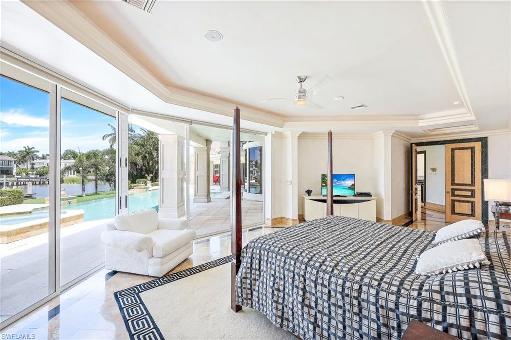 Furnished bedroom with a patterned bed and sliding doors overlooking a pool and canal.