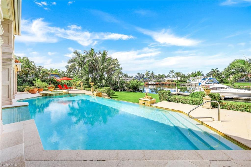 Swimming pool and stone patio overlooking a canal, with tropical landscaping and boats.