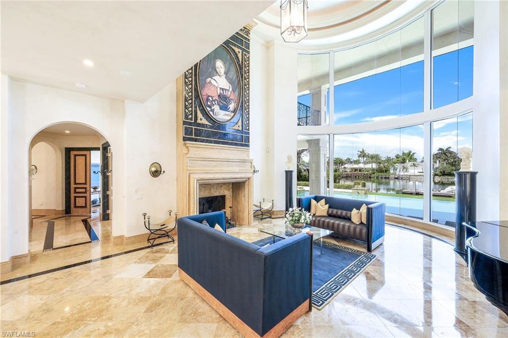 Living room with blue sofas, a marble fireplace, and tall windows overlooking the pool and water.