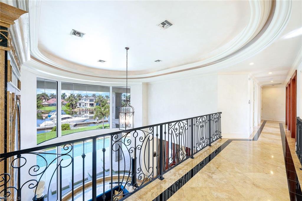 Upstairs gallery overlooking a foyer, with ornate railing and windows facing a pool and canal.
