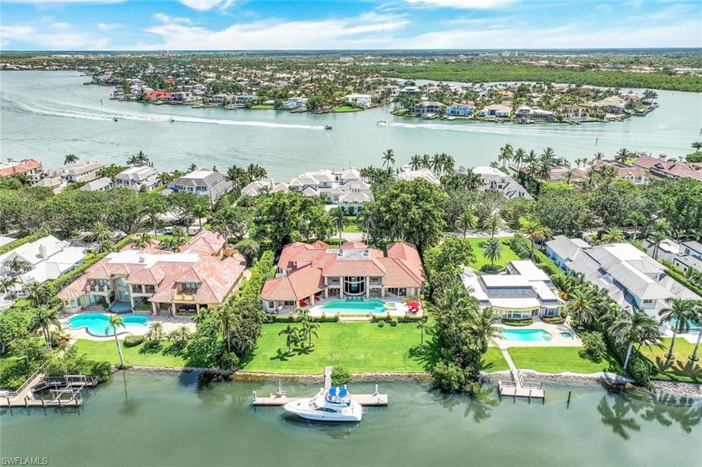 Waterfront home with a red tile roof, pool, expansive lawn, and boat dock beside a wide waterway.