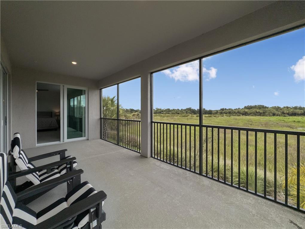 Covered balcony with striped chairs and black railing overlooking open marshland.