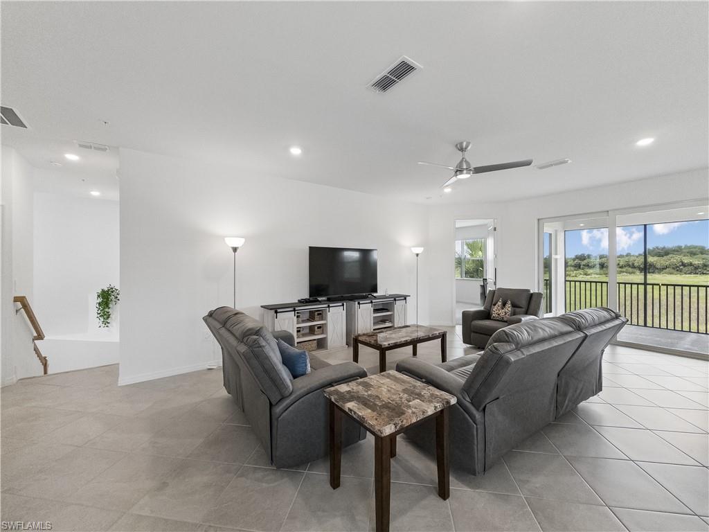 Furnished living room with gray seating, tiled floors, and sliding doors to a lanai overlooking greenery.