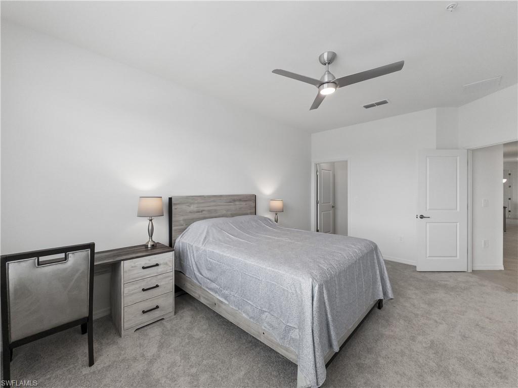 Bedroom with a gray bed, matching desk, carpet, and ceiling fan.