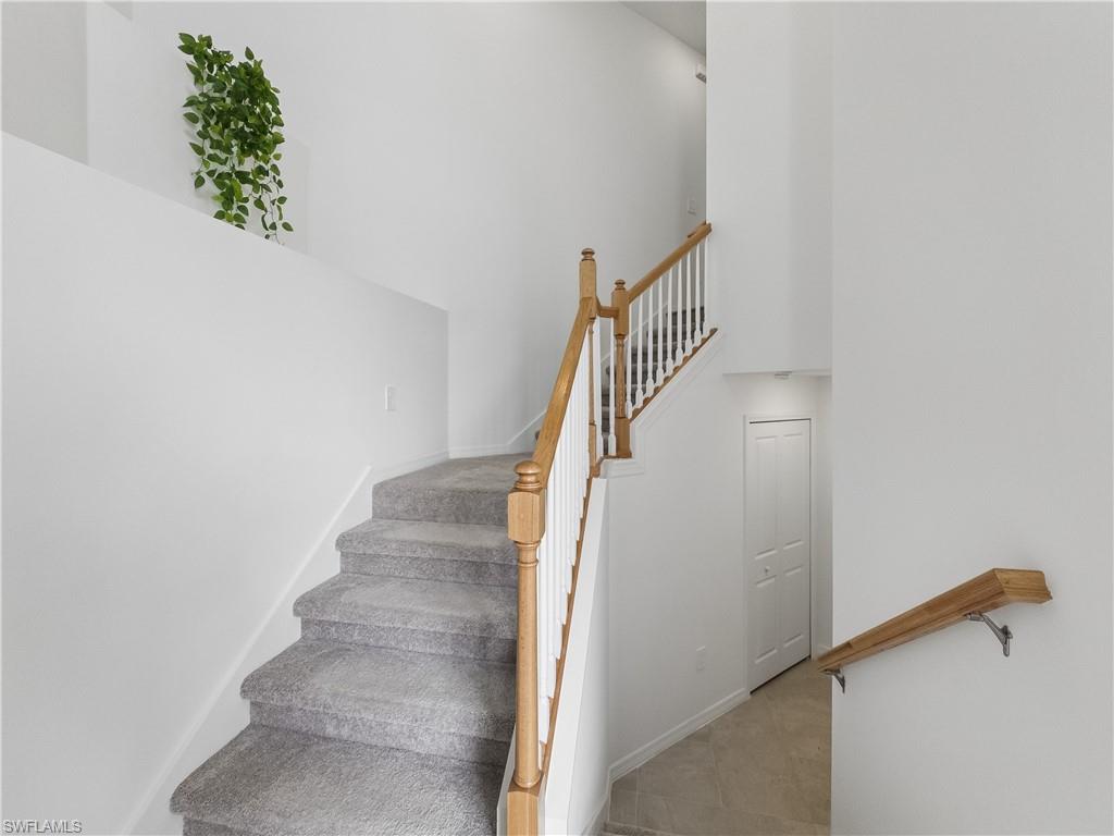 Carpeted interior staircase with white balusters, wood handrails, and a tiled lower landing.