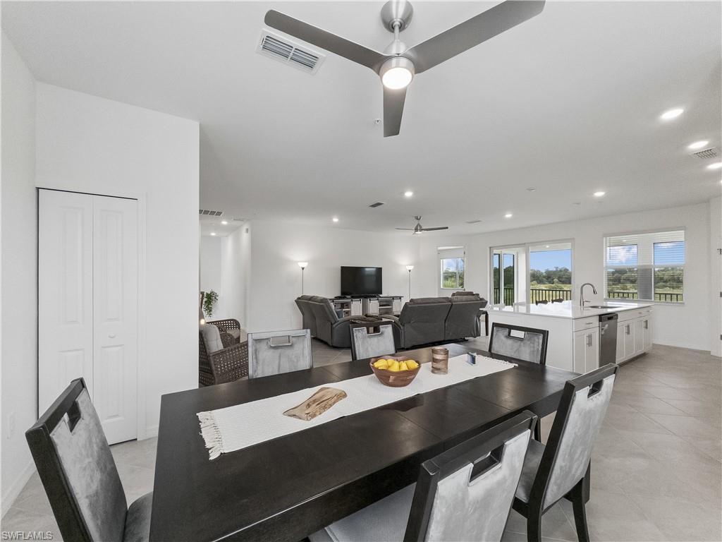 Dining area with a dark table, open to a white kitchen and living room with views of greenery.