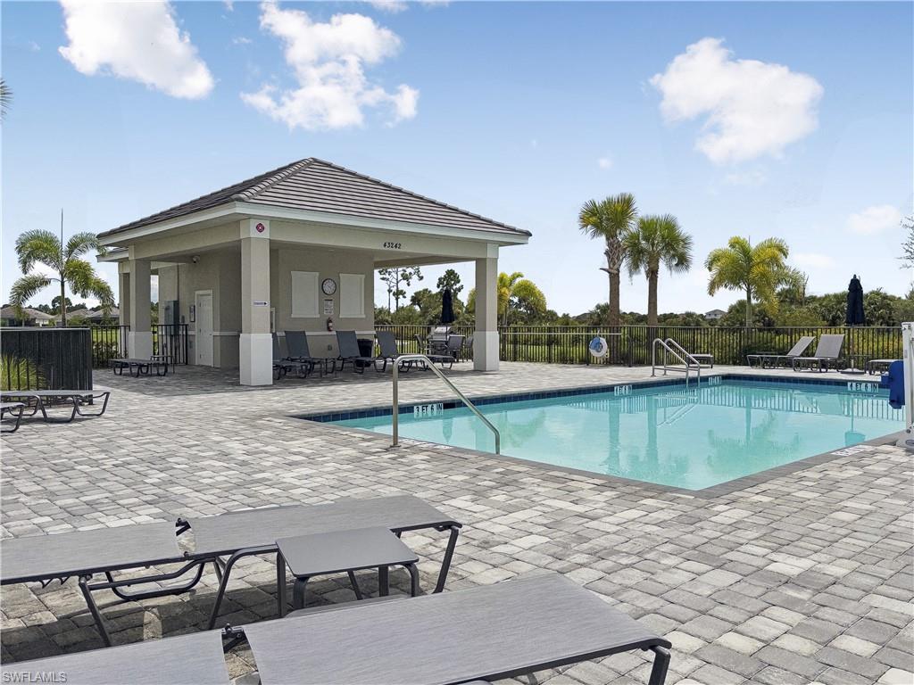 Community pool beside a covered pavilion, with palm trees and lounge chairs on a paved deck.