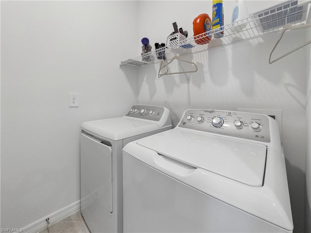 Laundry room with white top-load washer and dryer beneath a wire shelf of supplies.