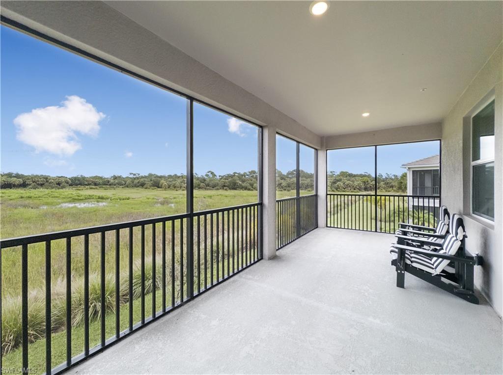 Screened lanai with striped chairs overlooking grassy wetlands and a tree line.